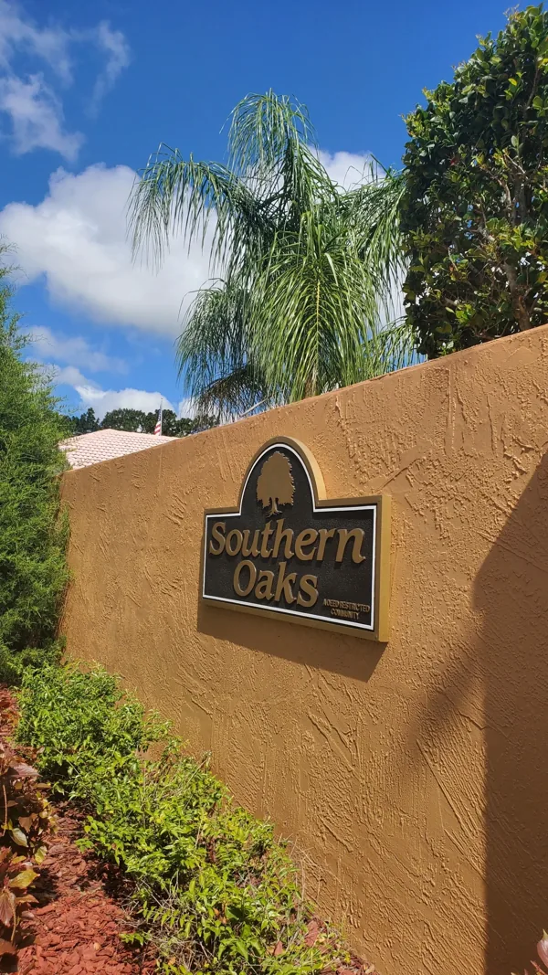 A sign on a wall that says `` southern oaks '' is surrounded by trees and bushes.